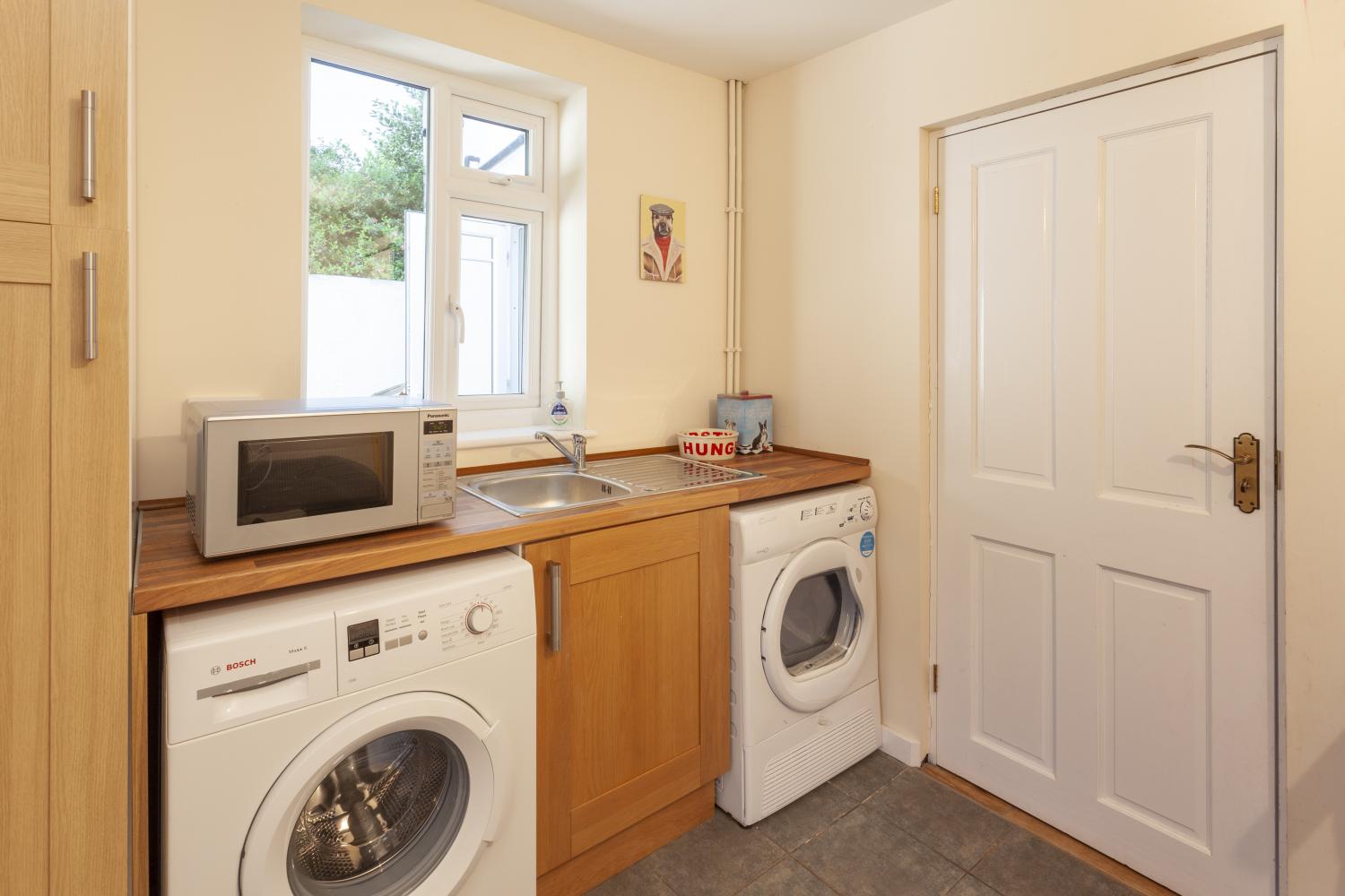 Large utility room with washing machine, tumble dryer, sink, microwave and separate cloakroom with toilet and basin.